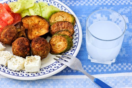Greek meze plate with grilled vegetables, meatballs, feta, salad and a glass of ouzo.
